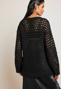 Pulover negru tricotat, cu un model geometral croșetat deschis, manșete și tiv cu margini ondulate, cu mâneci lungi și o croială lejeră.