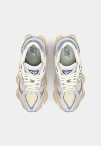 Light beige and blue sneakers featuring mesh and synthetic materials, rounded toe, thick midsole, and textured accents on the upper.