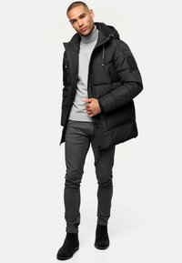 Sort vinterjakke med hætte, frontlynlås og tekstureret stof, båret over en grå turtleneck og sat sammen med grå skinny bukser og sorte støvler.