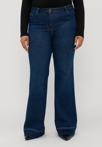 Jean bleu marine évasé en denim, avec une taille haute, des poches avant et des détails cousus à l'ourlet. Texture lisse.