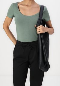 Grön kortärmad bodysuit med rundad hals, ihopparad med svarta högmidjade vida byxor och en strukturerad svart tote-väska.