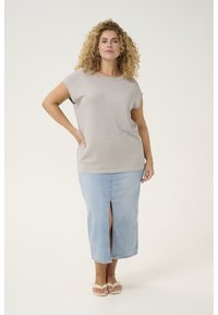 Beige kortærmet top med en subtil glans, parret med en lys blå denimnederdel med en frontslids. Sandaler fuldender looket.