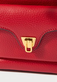 Borsa a mano in pelle rossa con superficie strutturata, chiusura in metallo dorato e design geometrico distintivo. Cuciture accentuate.