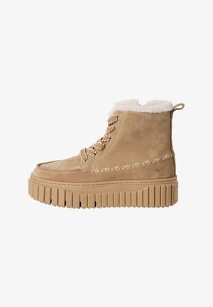 Beige Wildleder-Ankle-Boots mit einem samtigen Kunstfellkragen, dekorativen Nähten und einer dicken, geriffelten Sohle. Metallische Akzent-Schnürsenkel runden das Design ab.