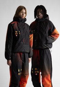 Melni jaku ar dzīvīgu oranžu gradients, kurās ir abstrakti raksti un kabatas ar rāvējslēdzējiem, saskaņotas ar atbilstošām biksēm.