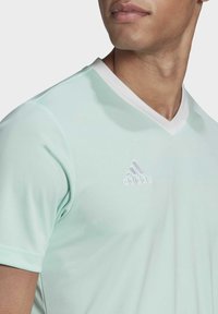 Sportovní tričko v mátově zelené barvě s výstřihem do V a bílým límečkem. Na přední straně se nachází bílé logo Adidas. Vyrobeno z hladké, lehké tkaniny.