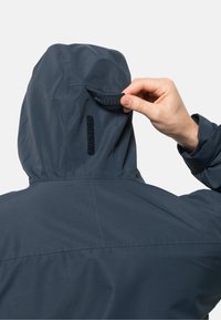 Donkerblauwe waterdichte jas met een gestructureerde capuchon. Verstelbare klittenbandriem aan de achterkant en verticale naaddetails. Hooggesloten ontwerp.