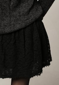 Svart spetskjol med blommiga mönster, med ett vågigt fåll och lager-textur, matchad med en mörk stickad tröja.