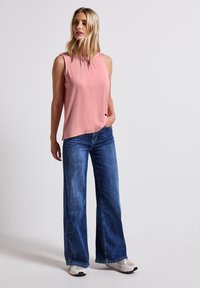 Top sans manches rose clair avec un col froncé, associé à un jean en denim bleu à jambes larges. Le modèle porte des baskets blanches. Tenue simple et décontractée.