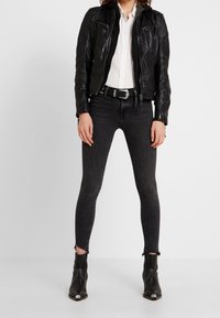 Veste en cuir noir au design ajusté, chemise blanche, jean skinny noir avec ourlet effiloché, et bottines noires avec accents argentés.