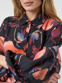 Czarna koszula w kwieciste wzory w odcieniach czerwieni, pomarańczu i niebieskiego. Posiada kołnierzyk oraz falbaniaste mankiety, wykonana z teksturowanej tkaniny.