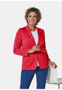 Rode zachte blazer met een getailleerd ontwerp, voorzien van een deskundig gelapt revers en voortassen, gecombineerd met een witte top en blauwe jeans.