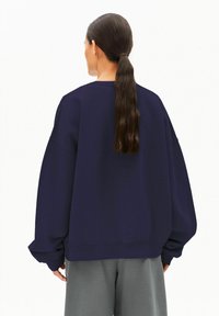 Marineblaues übergroßes Sweatshirt mit tief angesetzten Schultern und gerippten Bündchen, kombiniert mit hellgrauen Hosen. Glatter Stoff ohne sichtbare Muster.