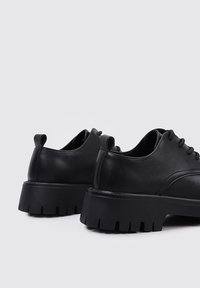 Zapatos de cuero negro con un diseño elegante, que cuentan con una suela gruesa y texturizada y bucles sutiles en el talón para facilitar su uso.