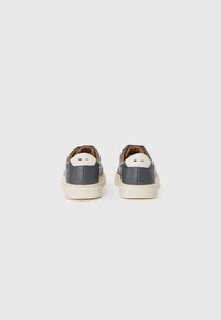 Grå lærersneakers med hvite såler, med en matt finish og et minimalistisk design. Brune detaljer på innsiden og baksiden av hælen.