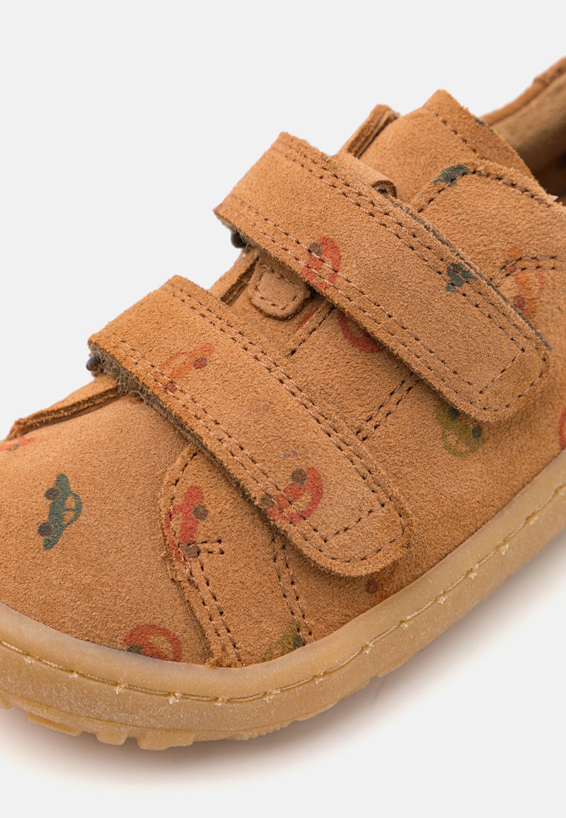 Beige Wildlederschuh mit zwei Klettverschlüssen, der ein verspieltes Muster aus bunten Formen aufweist. Runde Zehenkappe und rutschfeste Gummisohle.