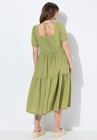 Grünes Midikleid aus strukturiertem Stoff, mit Puffärmeln, offener Rückenpartie mit Bindeband und einem schichtartigen Rockdesign, kombiniert mit Plateausandalen.