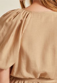 Beige linnen jurk met een ontwerp van gerimpelde pofmouwen, een soepele textuur en een licht getailleerde taille voor een ontspannen pasvorm.