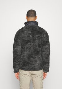 Pullover in pile di materiale nero testurizzato con colletto alto e accenti blu navy. Presenta una vestibilità comoda e polsi a costine, design posteriore semplice.