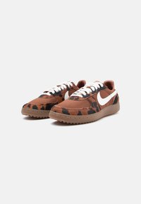 Tenisi din pânză maro cu imprimeu leopard negru și portocaliu, swoosh alb Nike, șireturi crem și talpă din cauciuc cu textură antiderapantă.