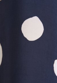 Tissu bleu foncé avec de gros pois blancs irréguliers, tissage texturé visible sur le matériau.