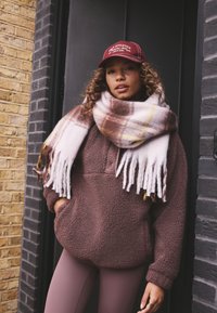 Brun fleece-tröja med en känguruficka, kompletterad med en stor, rosa fyrfärgad rutig halsduk med fransar.