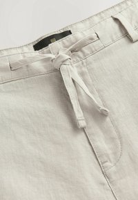 Pantaloni corti in lino beige chiaro con coulisse, tasche frontali e texture sottile. Design classico con dettagli di cucitura puliti.