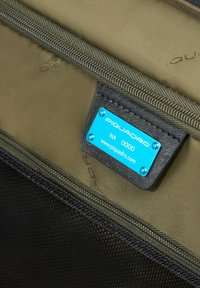 Interior de tela verde oliva con una cremallera negra texturizada y una etiqueta azul y plateada que dice "PIQUADRO NA 0000."