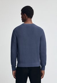 Marineblauwe gebreide trui met ribbeltextuur, lange mouwen en ronde halslijn, met een aansluitende zoom en manchetten.