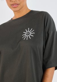 Dark gray cotton t-shirt with short sleeves and a round neckline. Features a white sun motif embroidered on the left chest area.