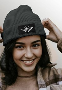 Black knit beanie with a textured pattern and a rectangular black patch featuring a silver star and winged design.