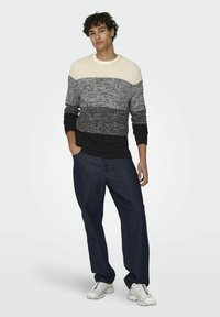 Maglione lavorato a maglia con righe orizzontali crema, grigio e nero; abbinato a jeans blu scuro e scarpe da ginnastica bianche.