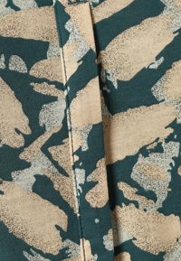 Tessuto mimetico verde e beige con una texture morbida, caratterizzato da dettagli di cucitura visibili e da una leggera variazione di colore.