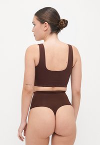Brun sømløs bralette med brede stropper og firkantet rygg, paret med høyt liv kortbukse-lignende undertøy med en glatt overflate.