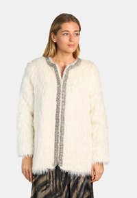 Chaqueta de piel sintética blanca con mangas largas, cuello redondo y cierre frontal adornado con cuentas plateadas a lo largo de los bordes.