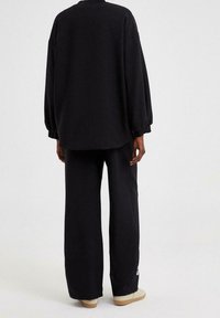 Schwarzes oversized Sweatshirt mit überschnittenen Schultern und langen Ärmeln, kombiniert mit weit geschnittenen schwarzen Hosen. Beide aus weichem Baumwollstoff gefertigt.