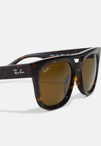 Ray-Ban aurinkolasit, joissa on kilpikonnakuosiset rungot, ruskeat linssit ja rohkea kulmikas muotoilu. Temppelin kohdalla on Ray-Ban-logo.