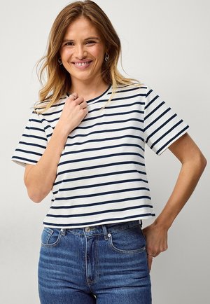 Maglietta in cotone a righe bianca e blu navy, con maniche corte e scollo rotondo. Abbinata a jeans in denim blu a vita alta.