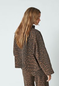 Brown leopard print oversized jacket with a collar, long sleeves, and textured fabric, paired with matching pants, viewed from the back.