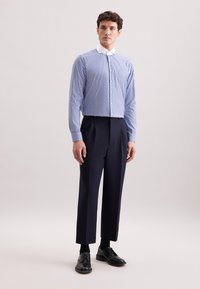 Camicia a righe blu chiaro con colletto alto, abbinata a pantaloni navy e scarpe nere stringate; vestibilità elegante e su фабbrica liscia.