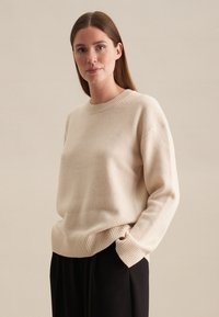 Beige gebreide trui met een ronde hals, geribbelde manchetten en zoom, met een zachte textuur en een relaxte fit, gecombineerd met donkere broeken.