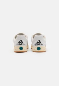 Baltas ādas sporta apavi ar teksturētu gumijas zoli, ietverot tirkīza akcentu uz papēža un melnu Adidas logo aizmugurē.