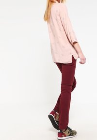 Chemise à manches longues rose clair avec des motifs d'étoiles argentées, associée à un pantalon slim-fit bordeaux et des baskets à motifs multicolores.