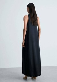 Black sleeveless maxi dress, flowy fabric with a smooth texture, long silhouette, and a loose fit, reaching mid-calf, with minimal design details.