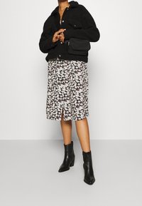 Svart fluffig jacka, blommig knälång kjol med slits, och svarta ankelboots. Liten svart väska bärs i crossbody. Strukturerade material.