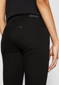 Jeans de denim negro con un ajuste de tiro medio, bolsillos traseros curvados, detalles de costura sutiles y un acabado de tela texturizada.