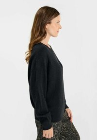 Maglione nero a maglia con vestibilità ampia, motivo testurizzato e maniche lunghe, abbinato a pantaloni con stampa leopardata. Vista laterale.