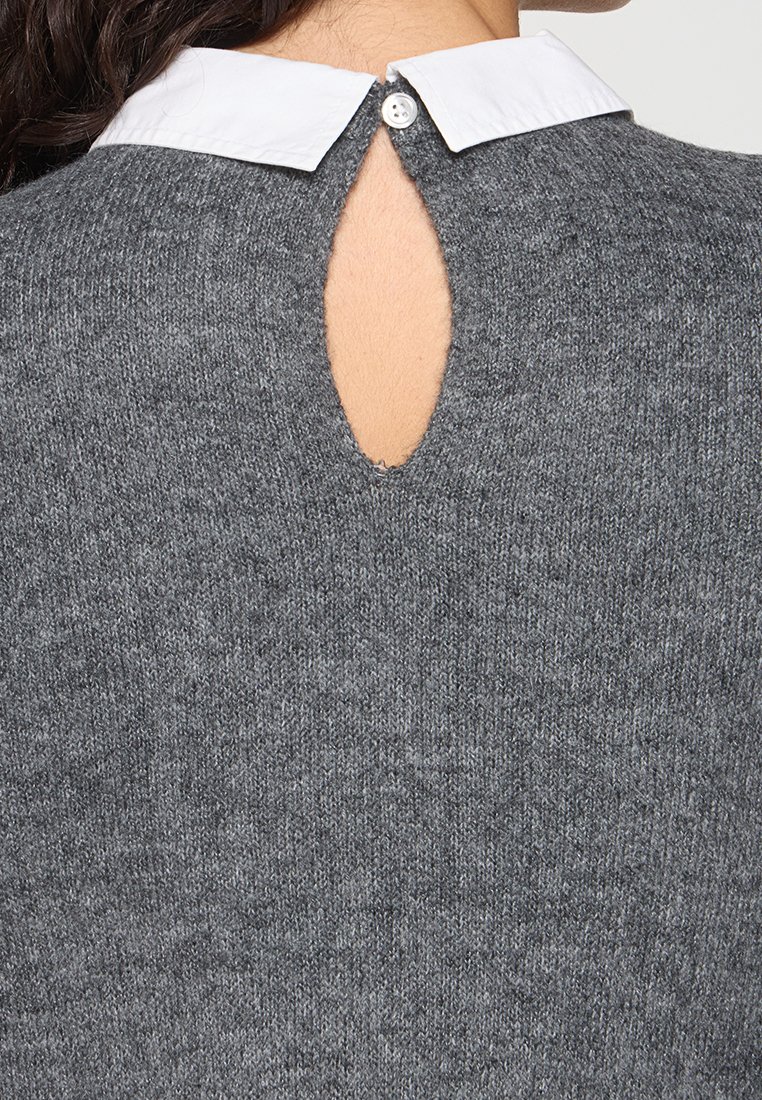 Grauer Strickpullover mit runder Schlüsselöffnung im Rücken und weißem Kragen mit Knopfverschluss. Weiche Textur mit einem lässigen Design.