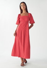 Koralna maksi obleka s kratkimi napihnjenimi rokavi, kvadratnim izrezom in prilegajočim se telesom. Narejena iz mehke tkanine z gladko teksturo. Preprost dizajn.