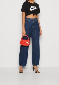 Camiseta negra corta con logo blanco de Nike, jeans de tiro alto y pierna ancha en azul, bolso rojo de charol y tacones altos negros con tiras.